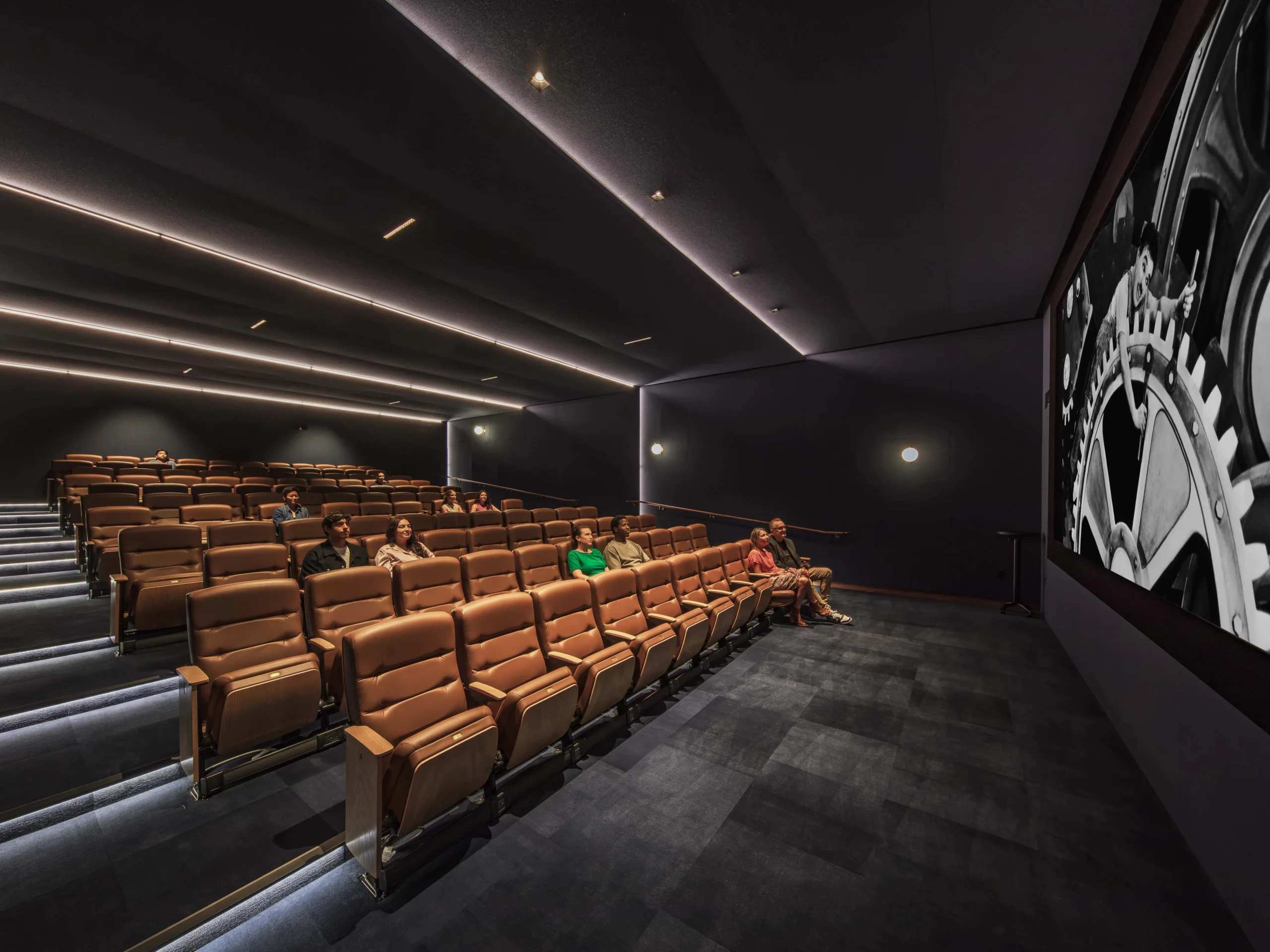 6 rows of brand new beige theater seats in a new movie theater, about 11 people scattered in the seats watching Chaplin's Modern Times.